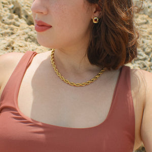 Gold rope chain necklace and gold and red studs on girl sitting at the beach